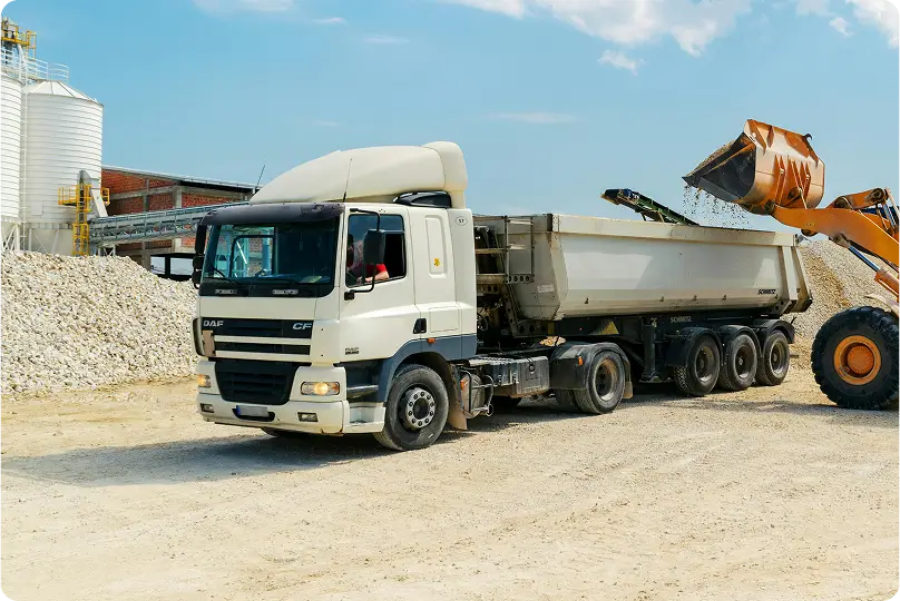 Rectangle 6 (1) Camião basculante branco a ser carregado por máquina escavadora amarela num estaleiro de construção.